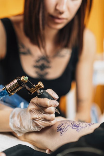 Female tattoo artist tattooing man’s arm in studio